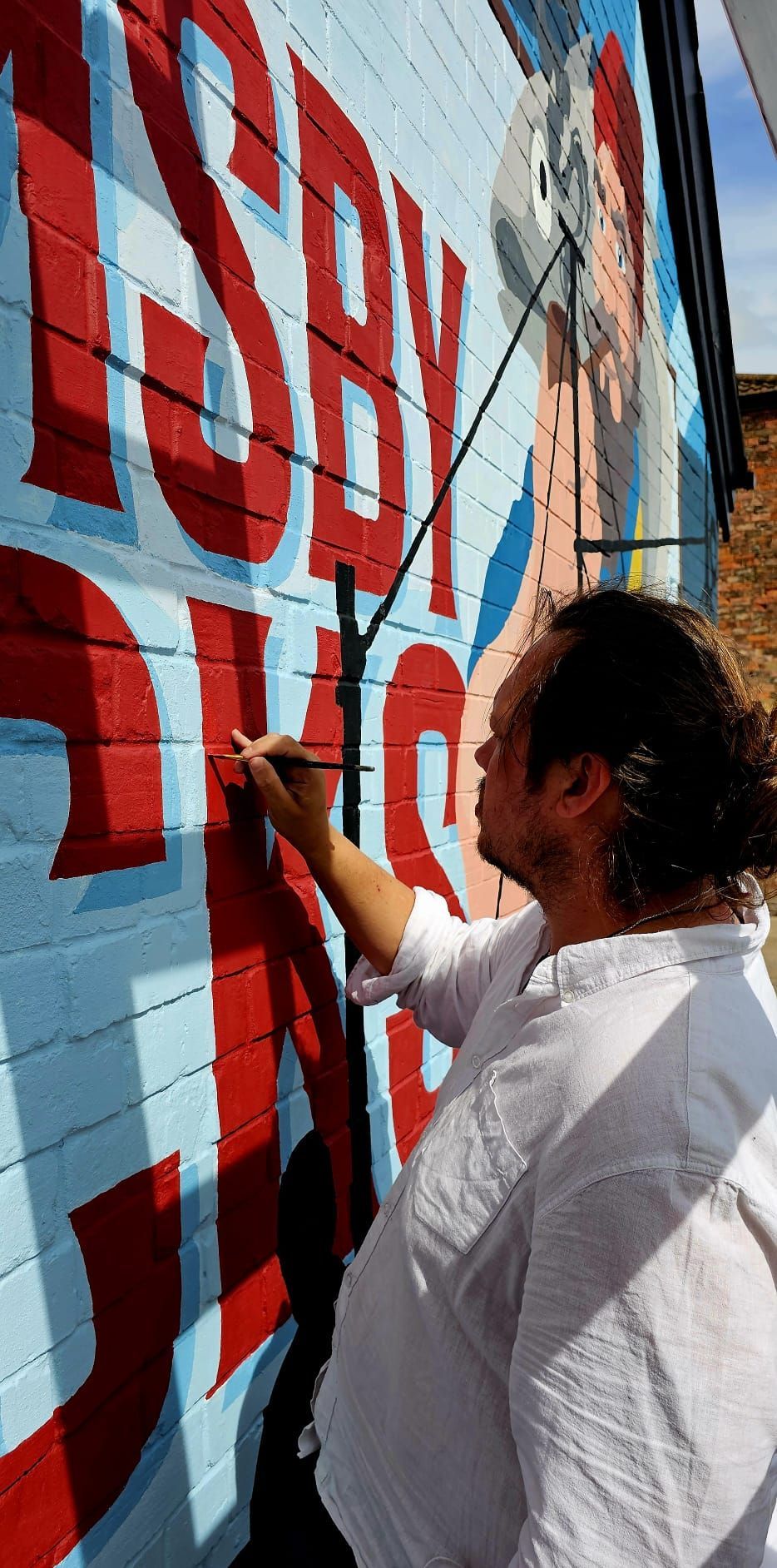 A man is painting a mural on a brick wall.
