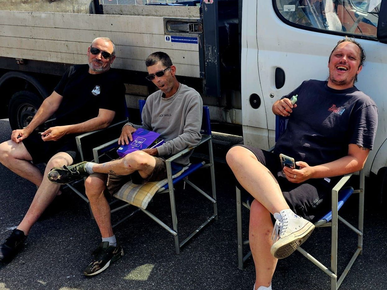 Three men are sitting in director 's chairs in front of a truck
