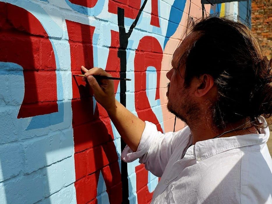 A man is painting a mural on a brick wall