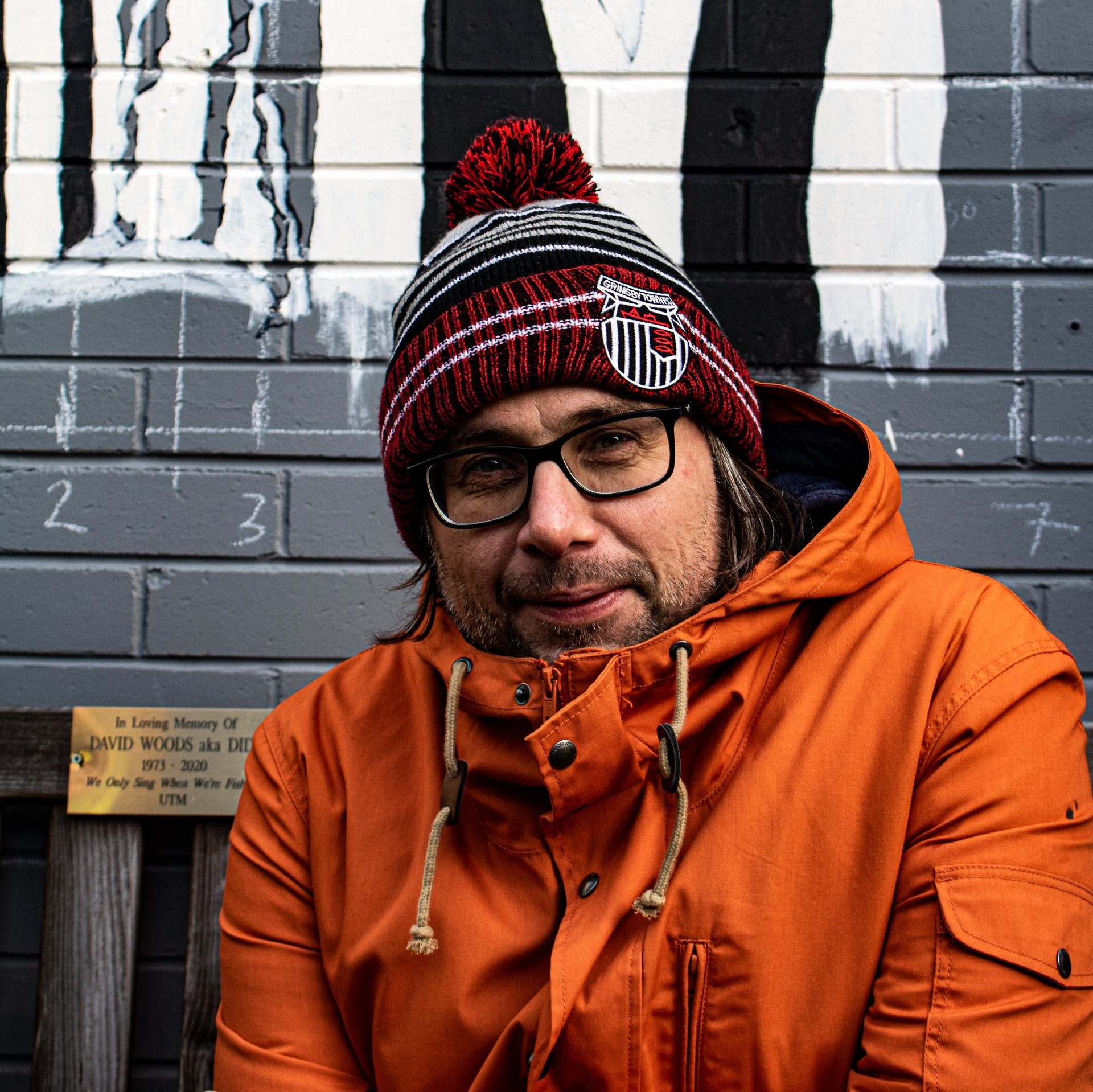 A man wearing a beanie and glasses is sitting on a bench