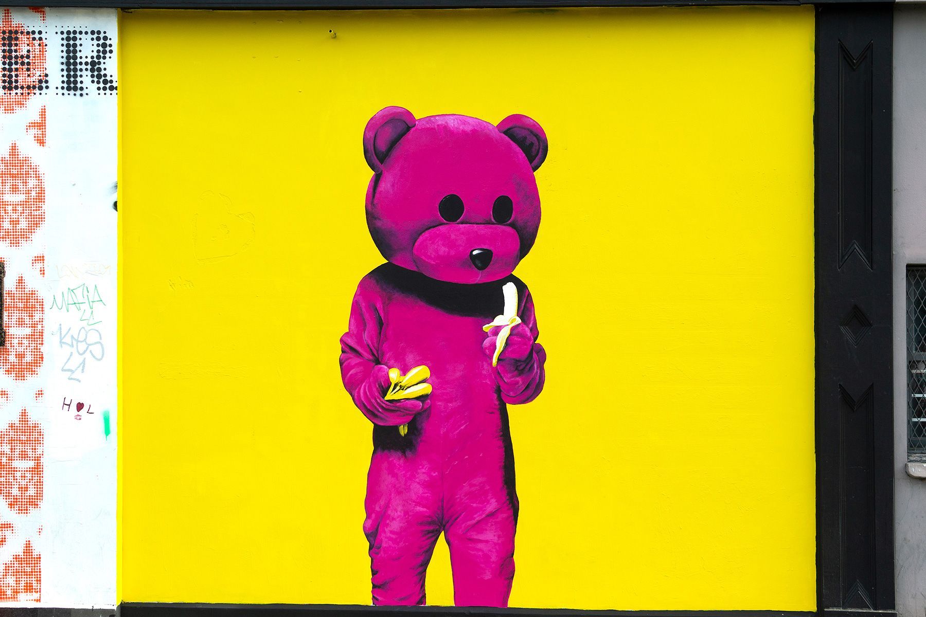 A pink teddy bear is holding a banana on a yellow background.
