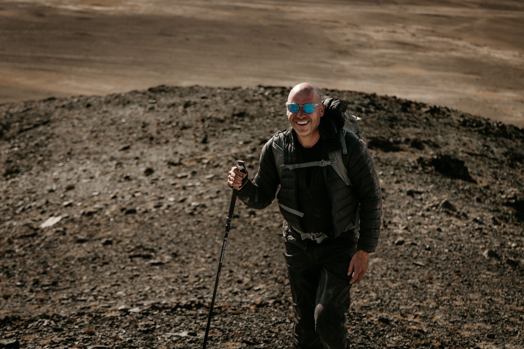 A man wearing sunglasses and a backpack is hiking in the desert.