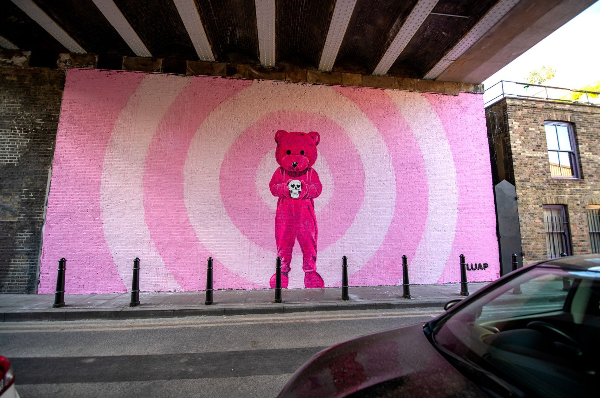 A pink teddy bear is painted on a wall under a bridge