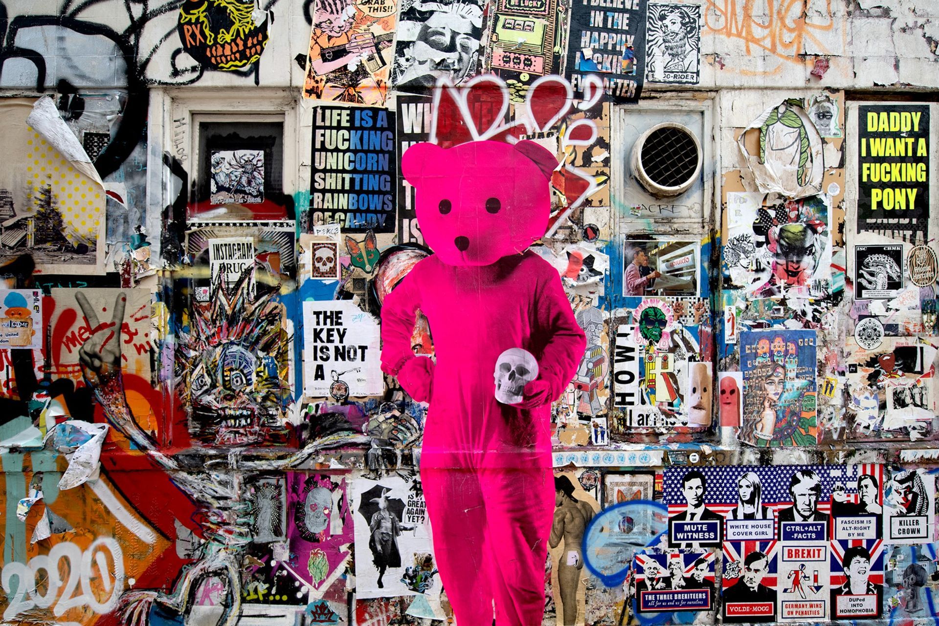 A pink teddy bear is standing in front of a wall covered in stickers.