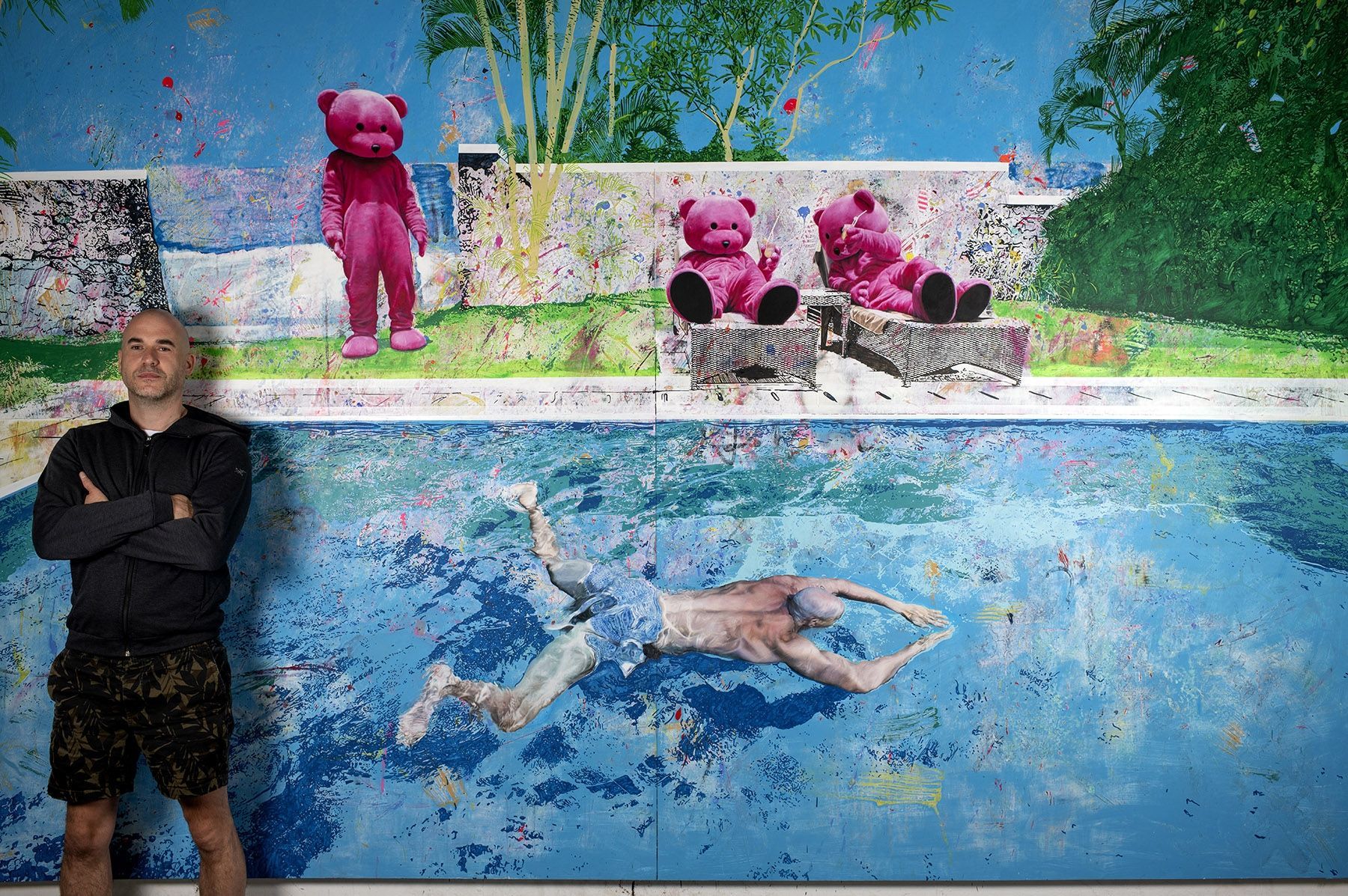A man is standing in front of a painting of a man swimming in a pool.