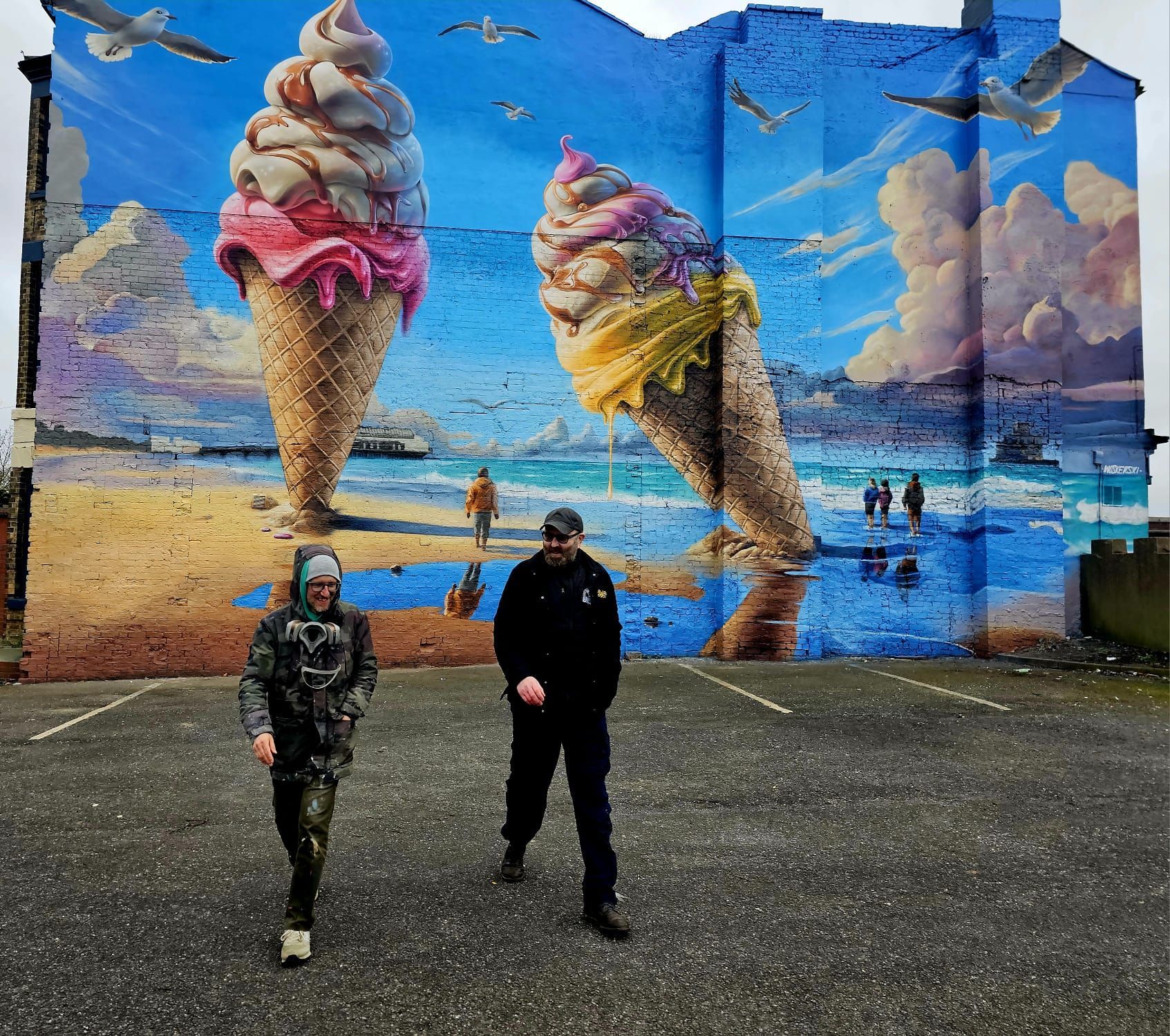 Two people standing in front of a large mural of ice cream cones