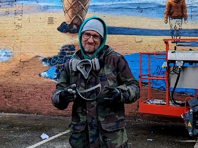 A man wearing headphones and a mask is standing in front of a mural.