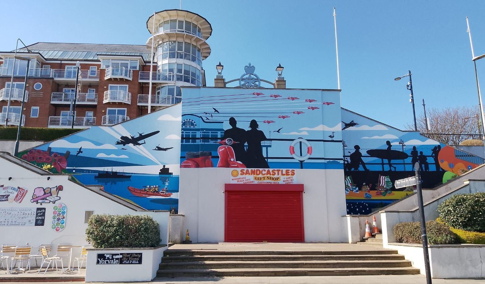 A large mural on the side of a building shows people walking on a pier