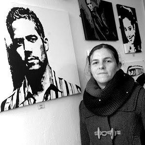 A woman is standing in front of a painting of a man.