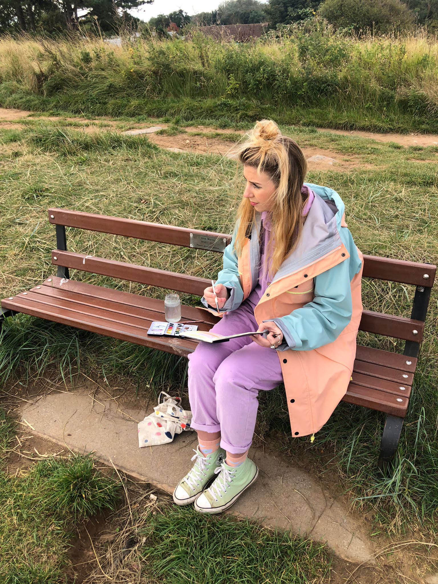 A woman is sitting on a park bench writing in a notebook.