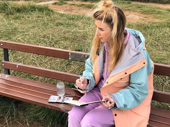 A woman is sitting on a park bench painting with watercolors.
