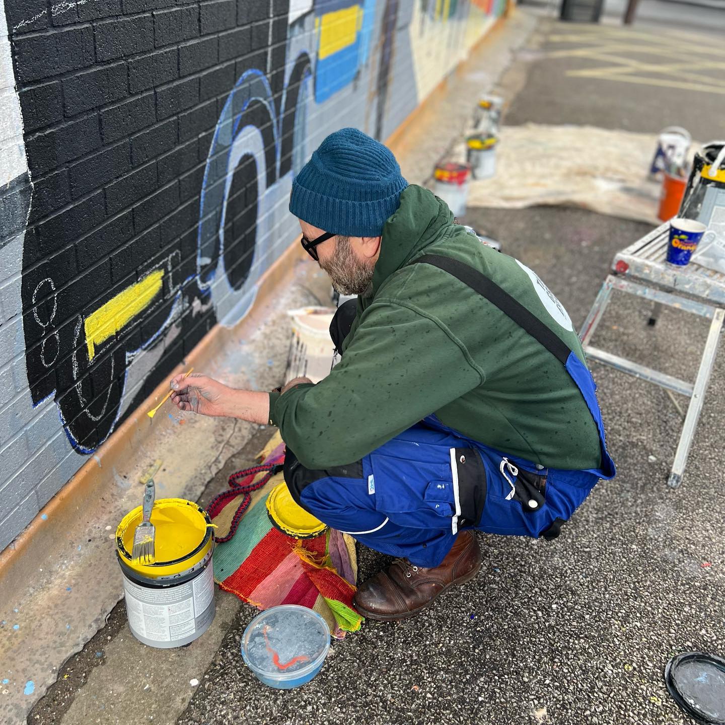 A man is kneeling down and painting a mural on a wall.