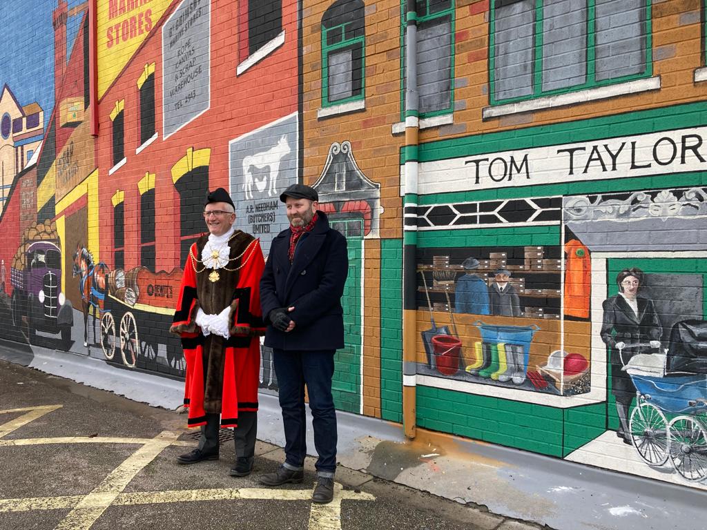 Two men are standing in front of a mural on the side of a building.
