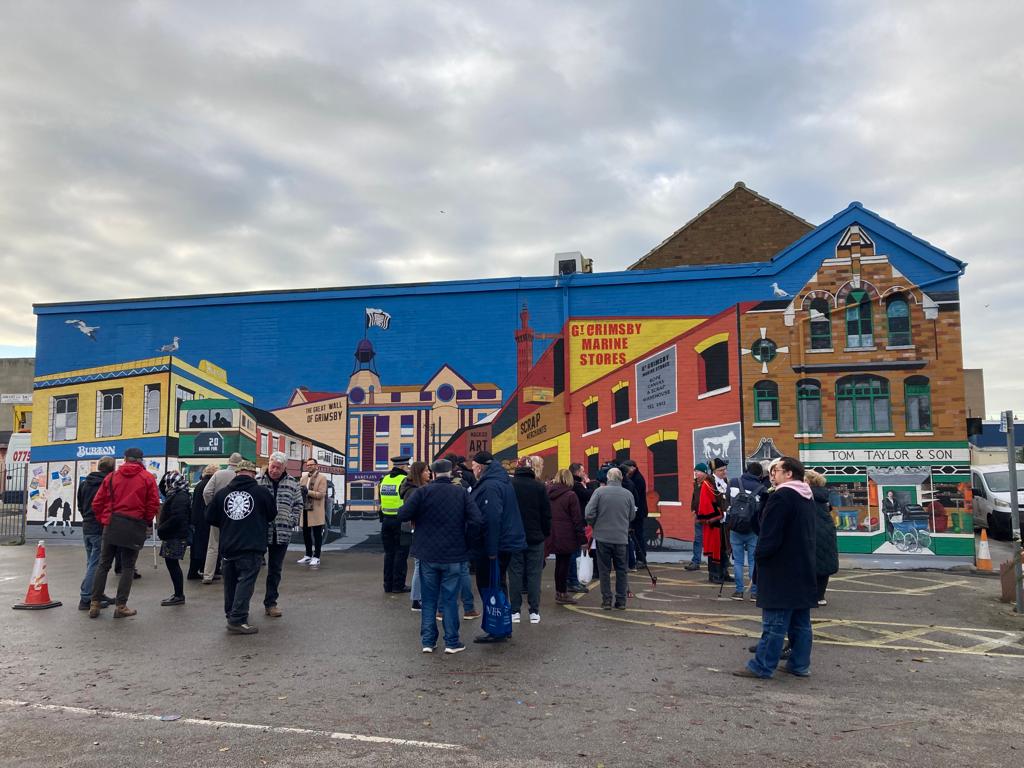 A group of people are standing in front of a building with a mural on the side.