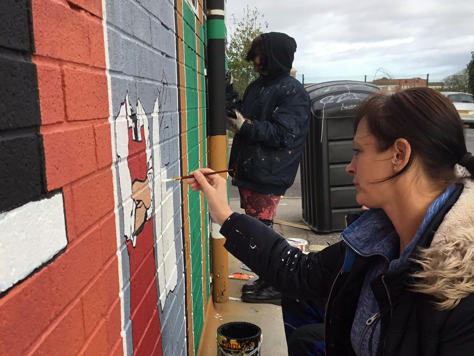 A woman is painting a picture of santa on a brick wall