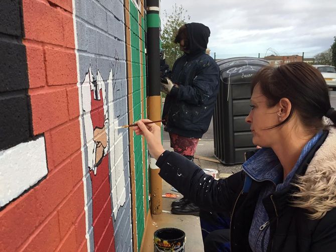 A woman is painting a picture on a brick wall