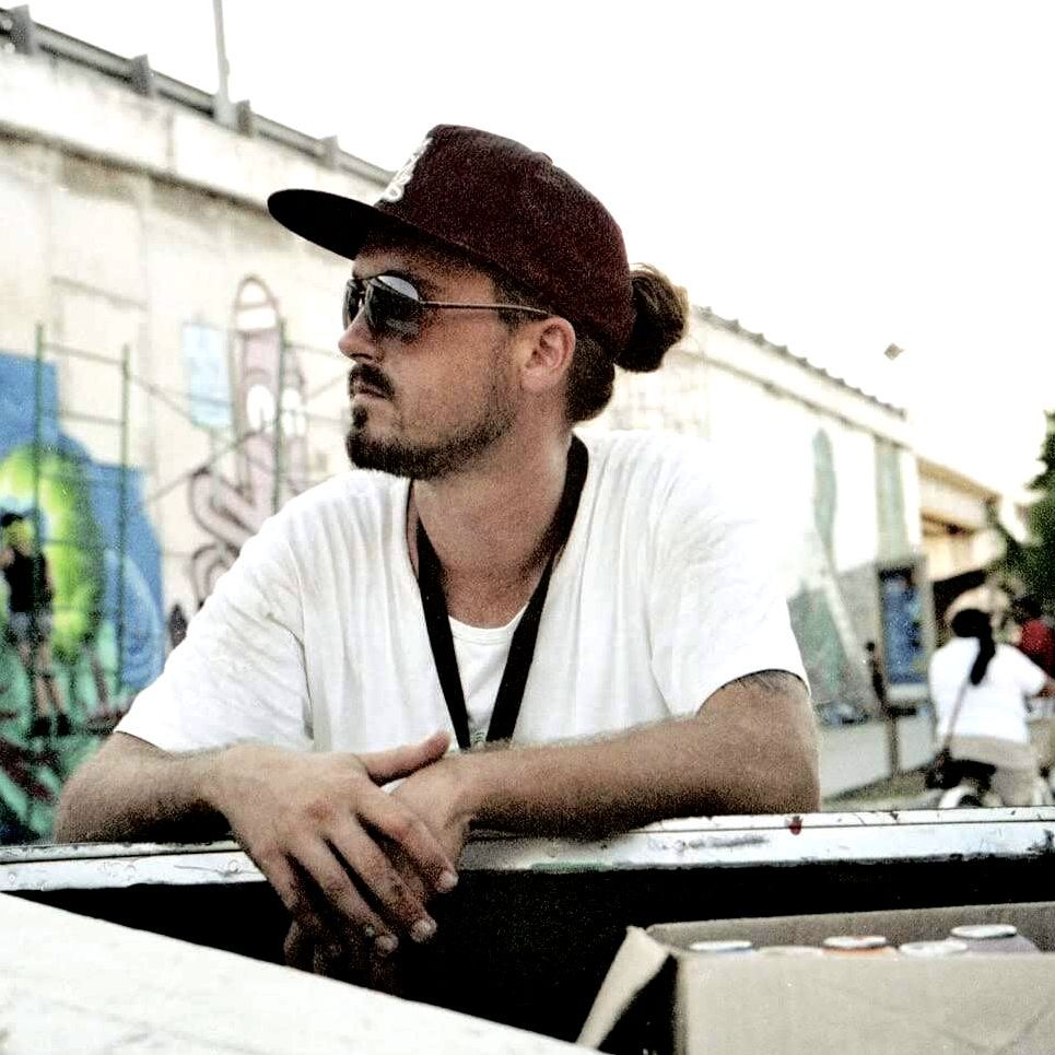 A man wearing a hat and sunglasses is leaning on a railing