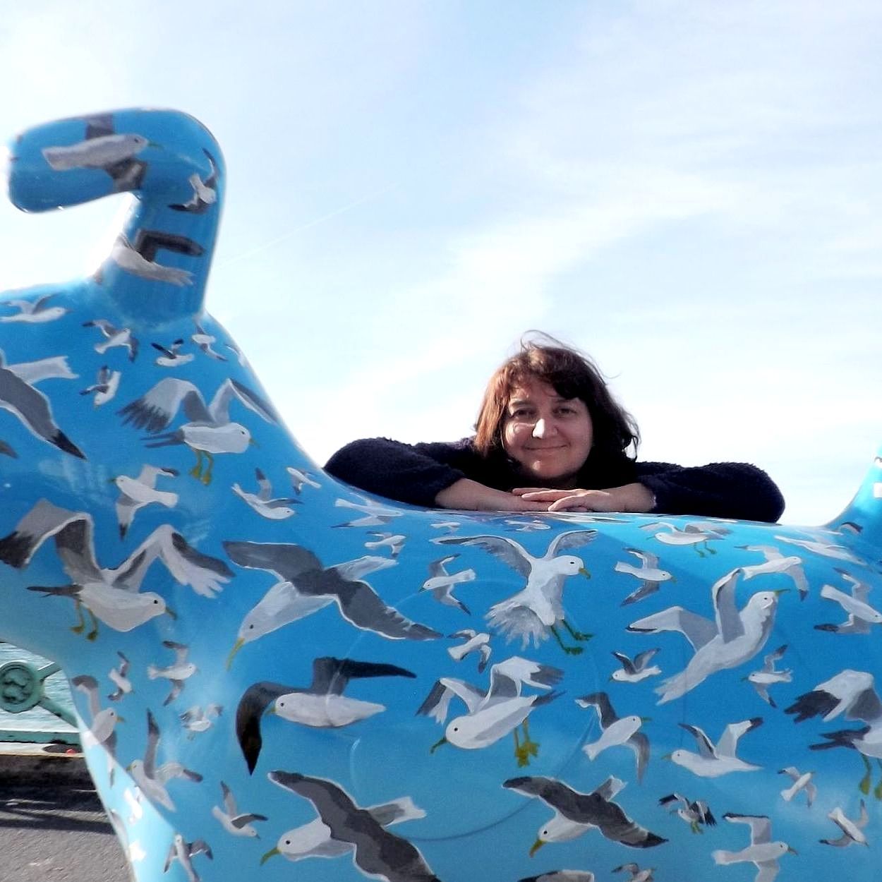 A woman laying on top of a blue statue with seagulls on it