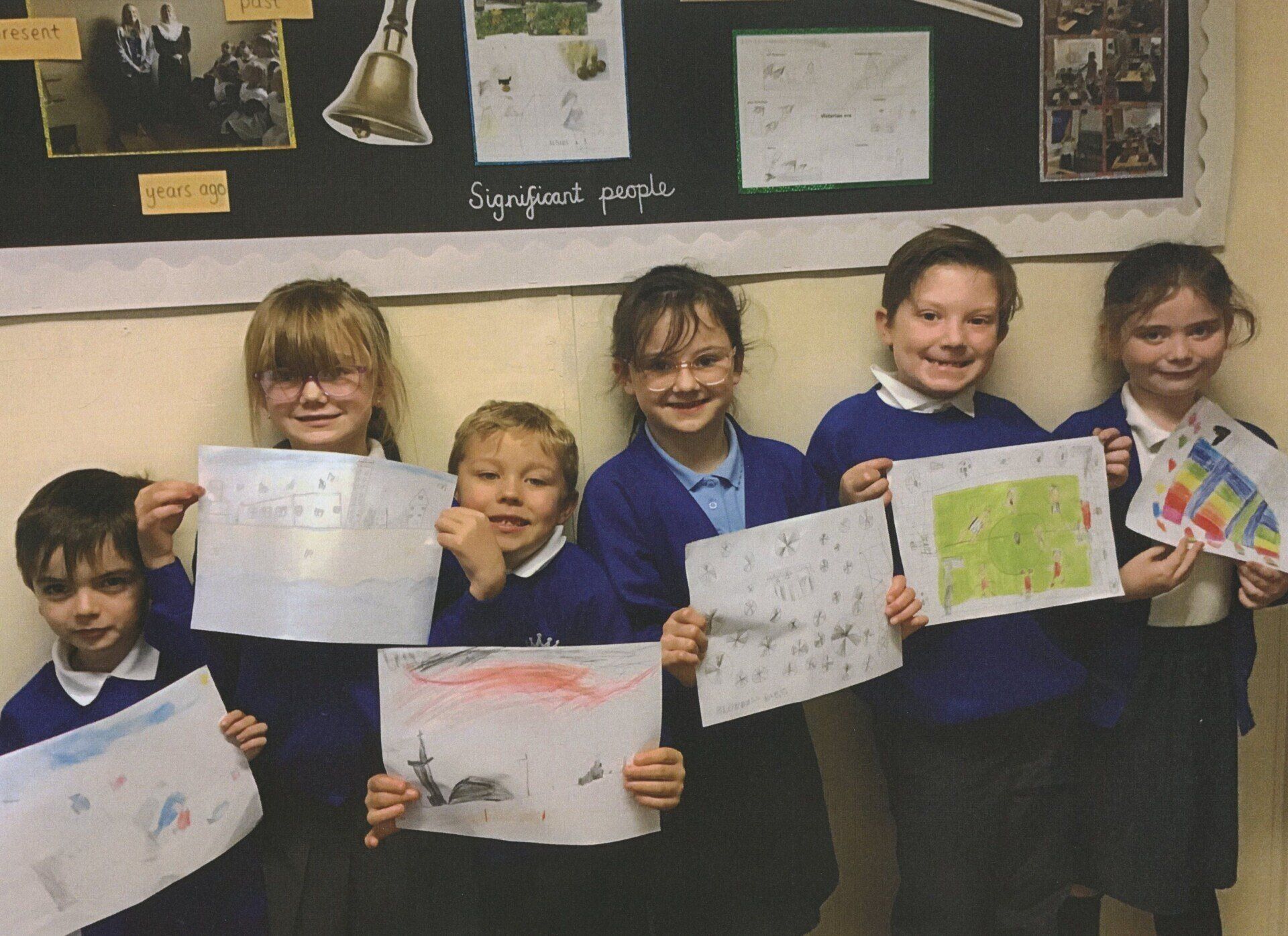A group of children are holding up their drawings in front of a bulletin board that says comfort people