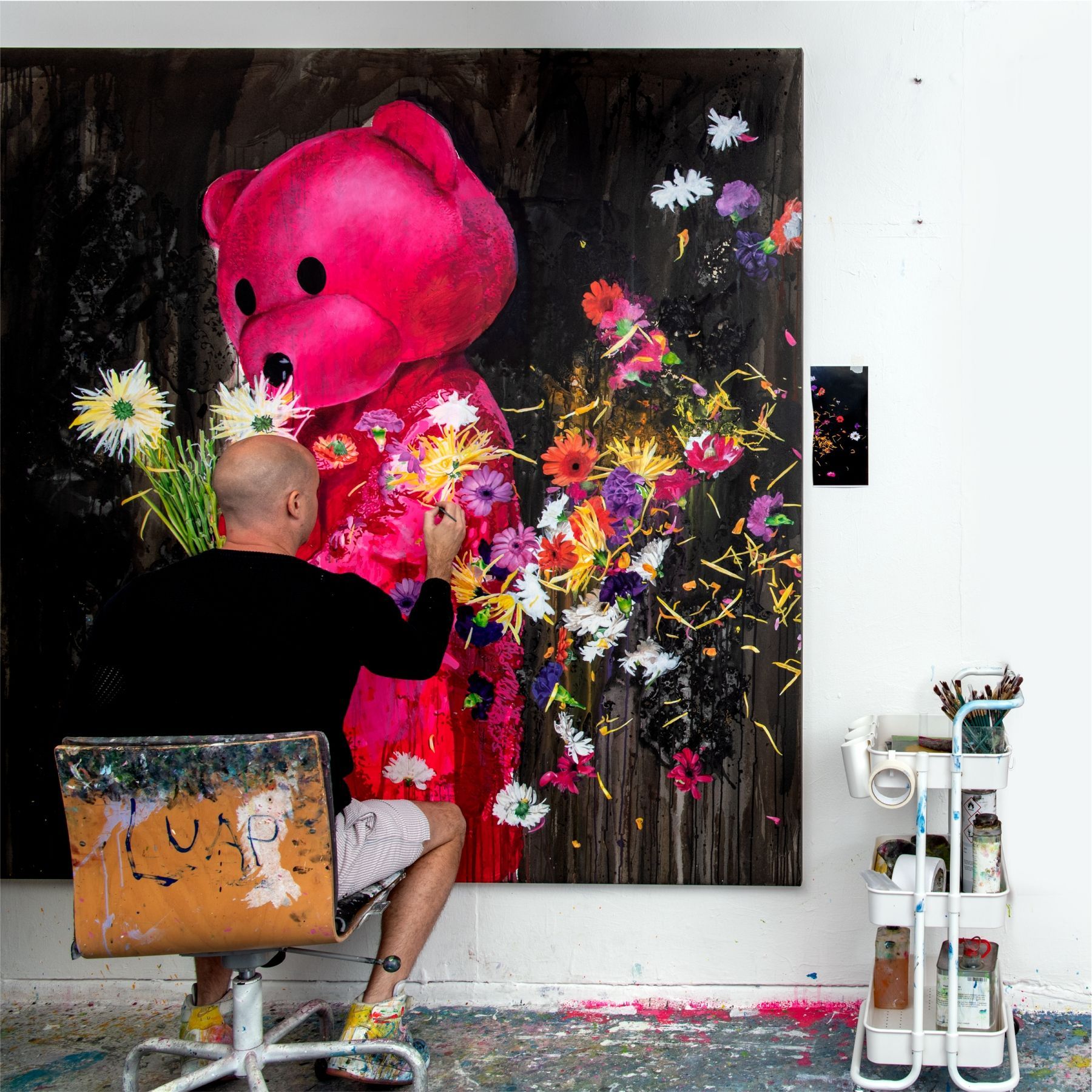 A man is painting a pink teddy bear with flowers