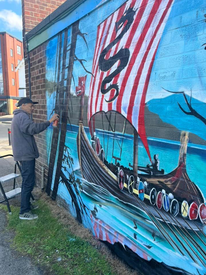 A man is painting a mural of a viking ship on the side of a building.