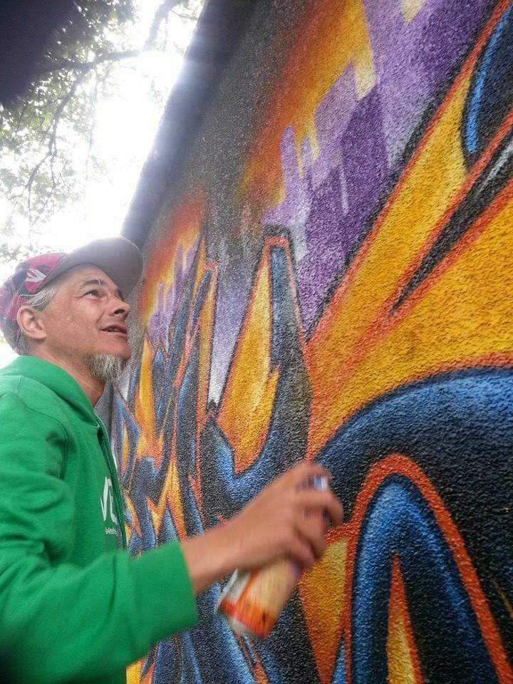 A man in a green hoodie is spray painting graffiti on a wall