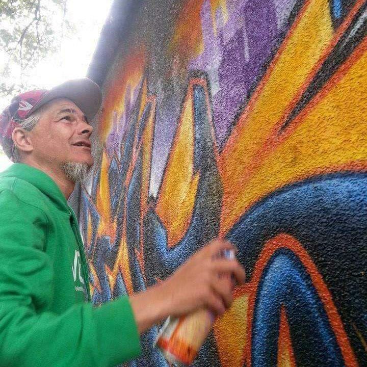 A man in a green jacket is spray painting graffiti on a wall.