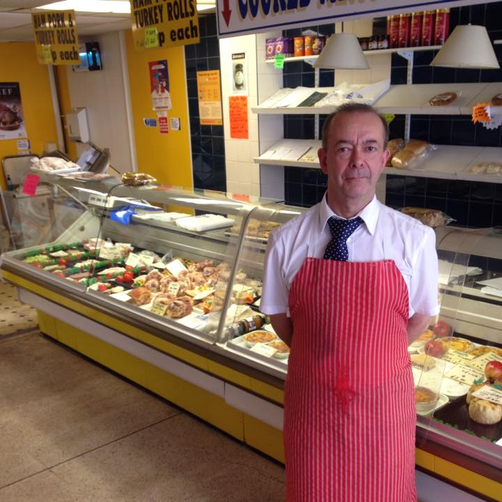 A man in a red apron stands in front of a display case in a store