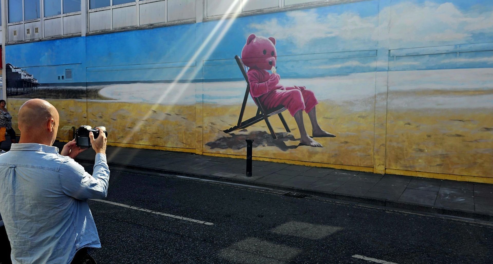 A man is taking a picture of a teddy bear sitting on a beach chair.