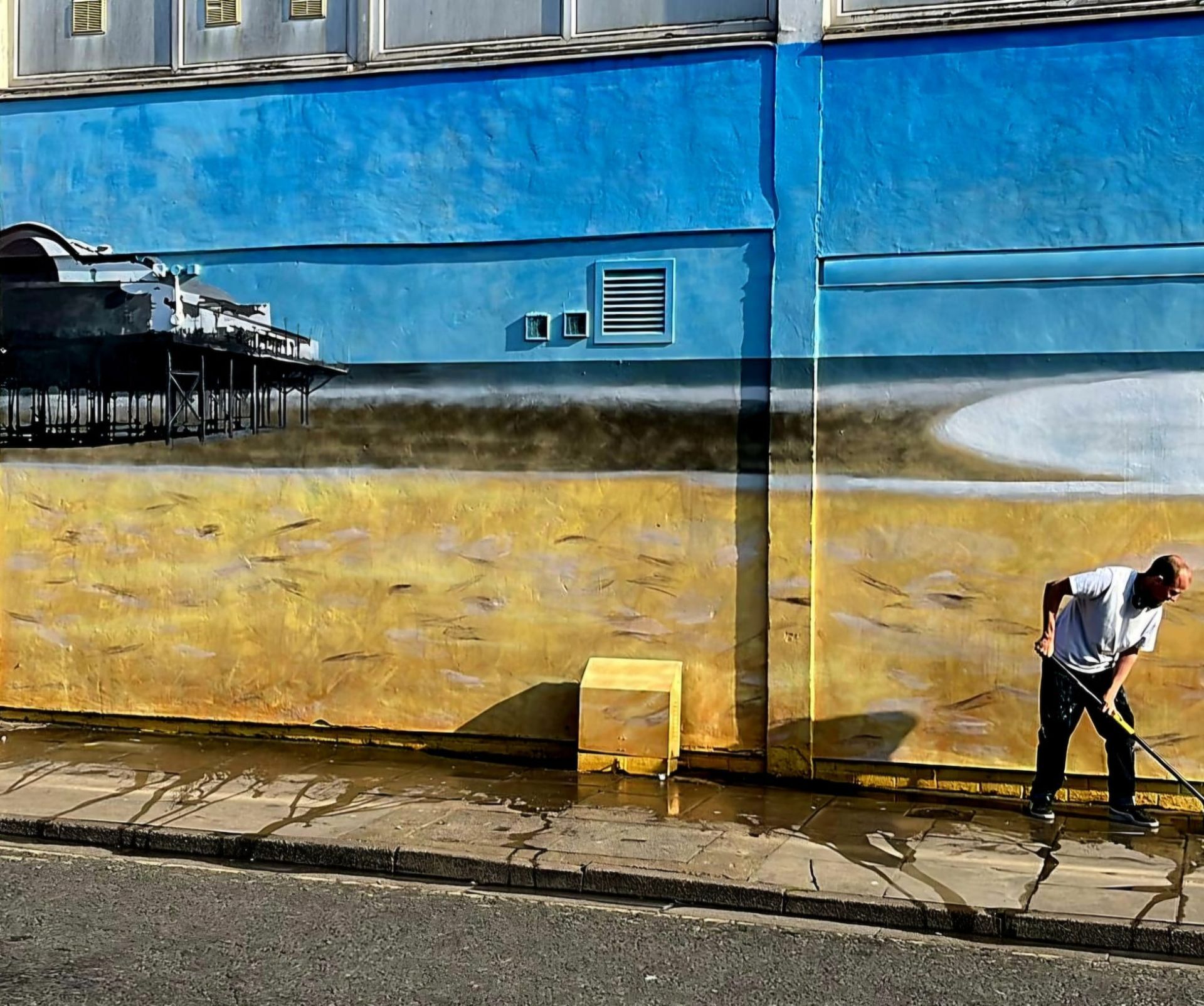 A man is cleaning the sidewalk in front of a mural