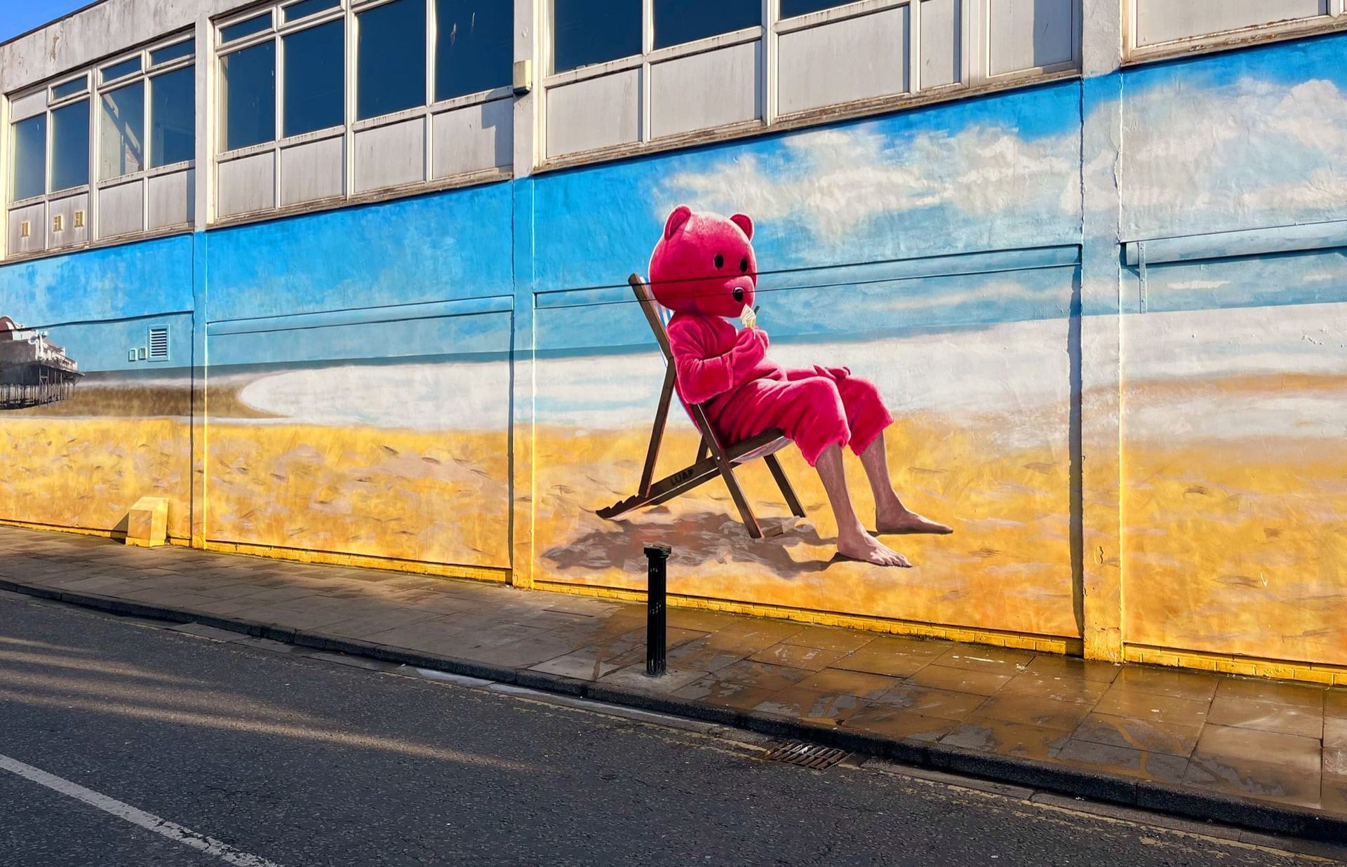 A pink teddy bear is sitting in a beach chair on a wall.
