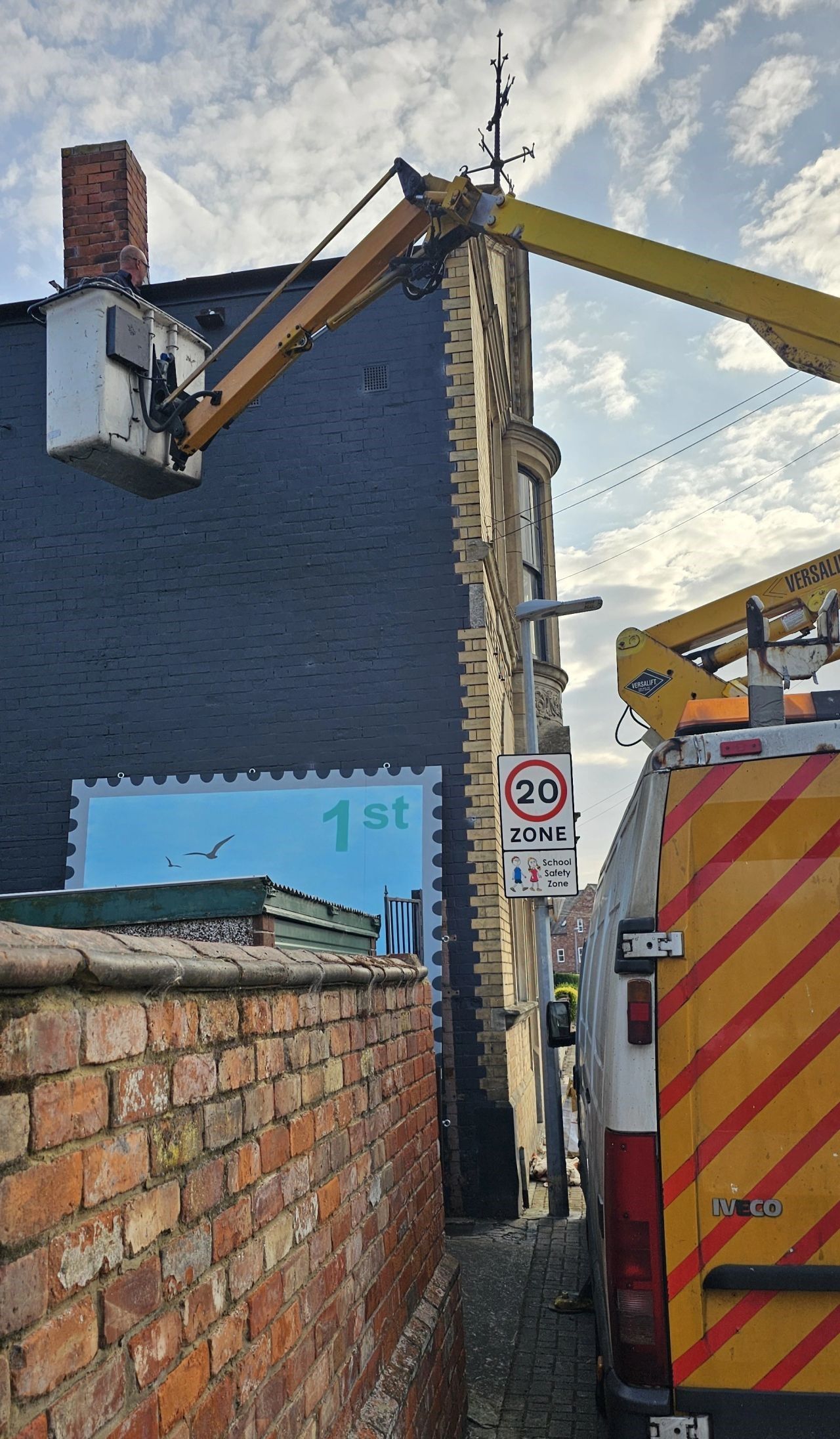 A yellow and red van is parked next to a brick wall.