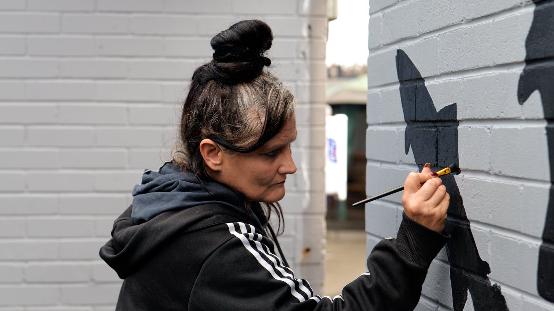 A woman is painting a picture on a brick wall.