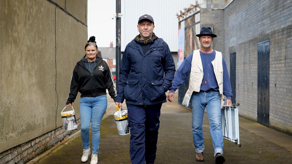 A group of people are walking down a street holding buckets of paint.