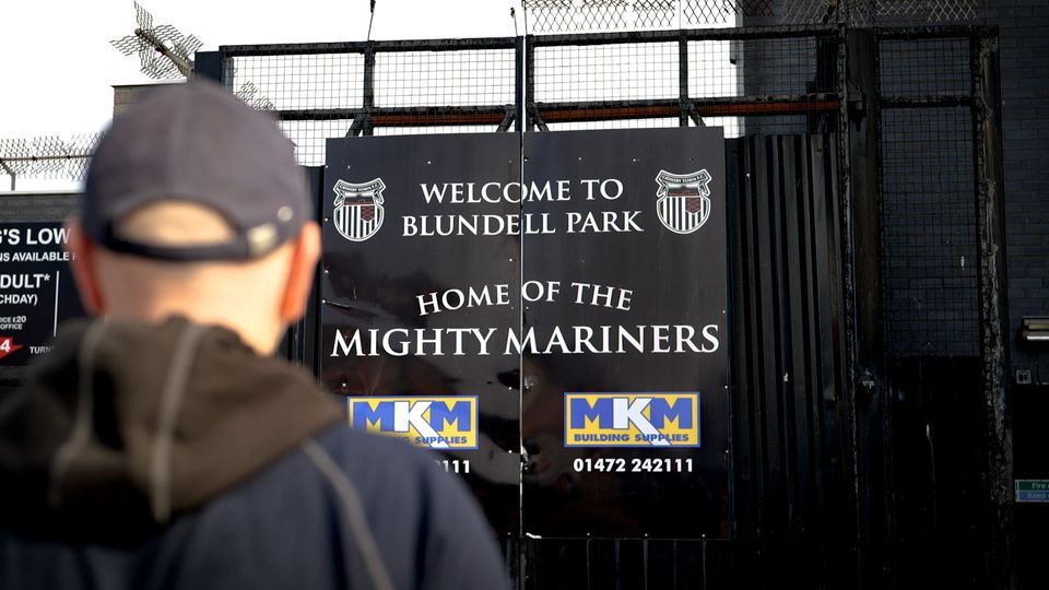 A man stands in front of a sign that says welcome to blunderl park home of the mighty mariners