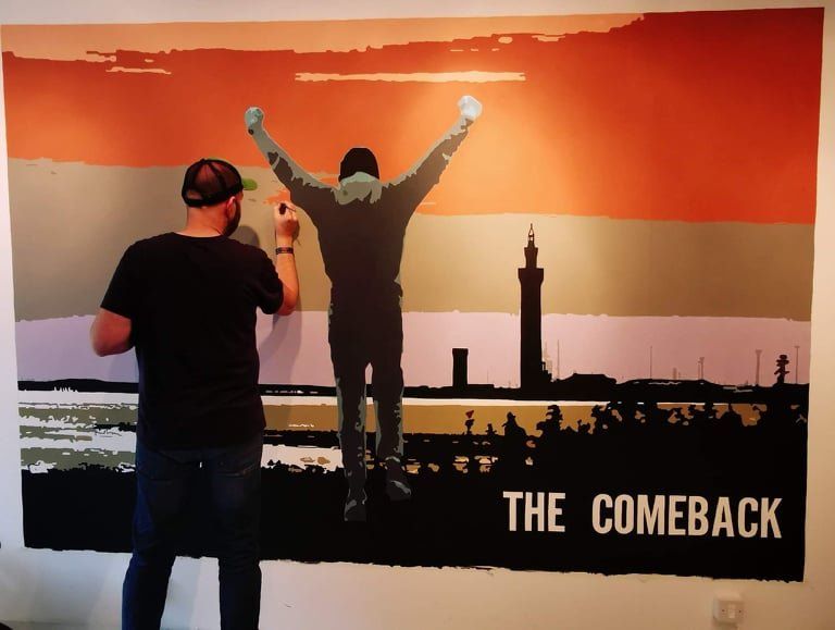 A man is painting a picture of a man with his arms in the air and the words