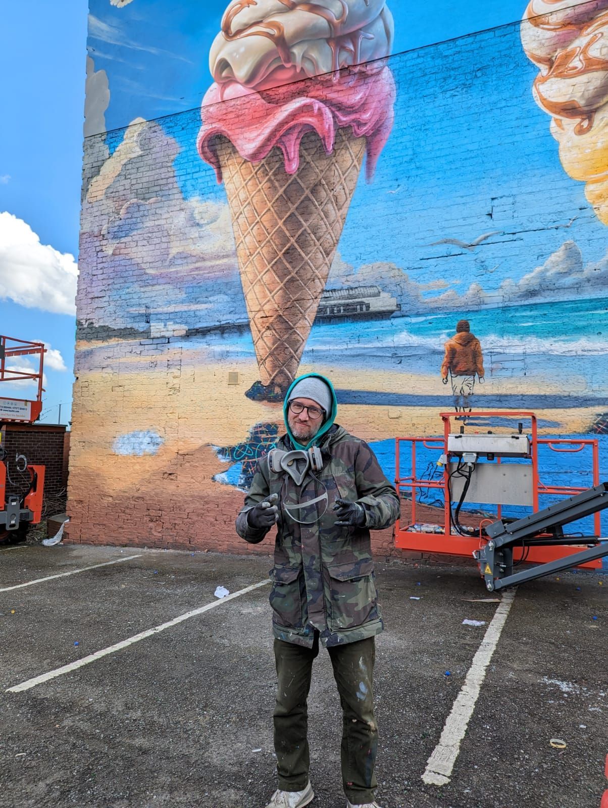 A man is standing in front of a large mural of an ice cream cone.