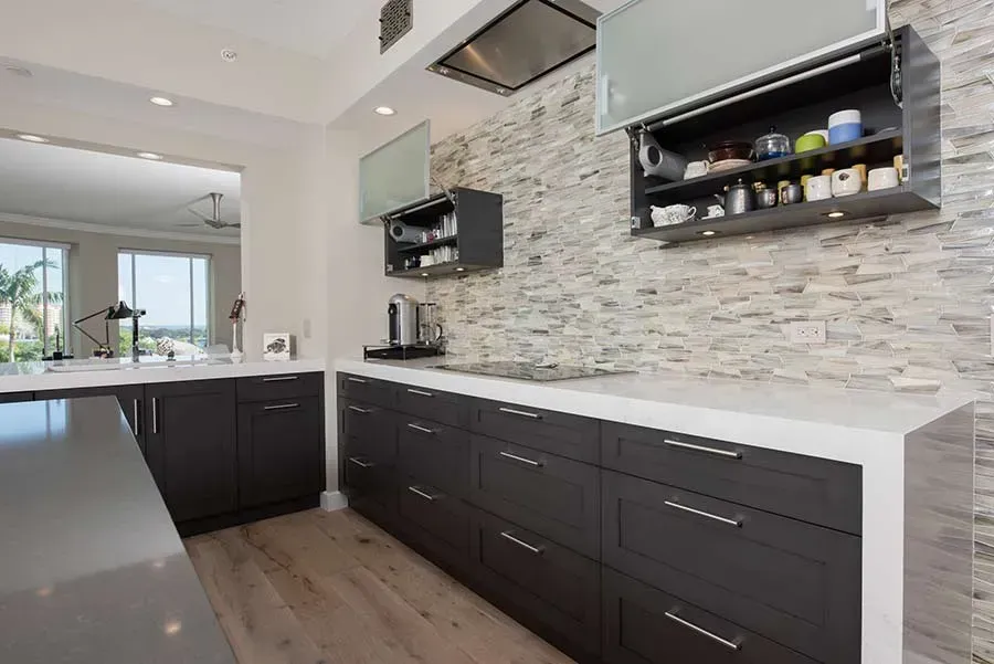 A kitchen with black cabinets and a stone wall.