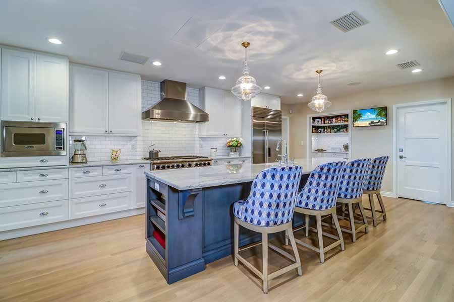 A kitchen with white cabinets , a blue island , and blue chairs.