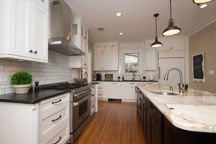 A kitchen with white cabinets , black counter tops , stainless steel appliances and a large island.