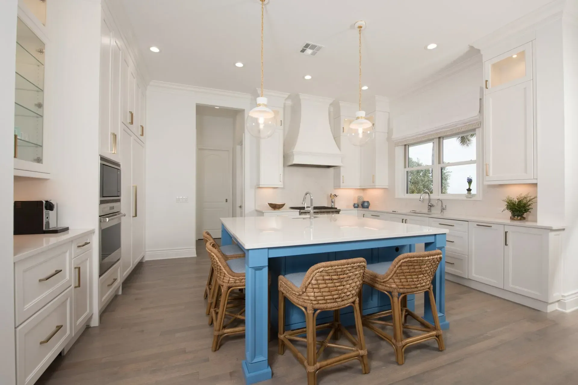 A kitchen with white cabinets and a blue island with wicker chairs.