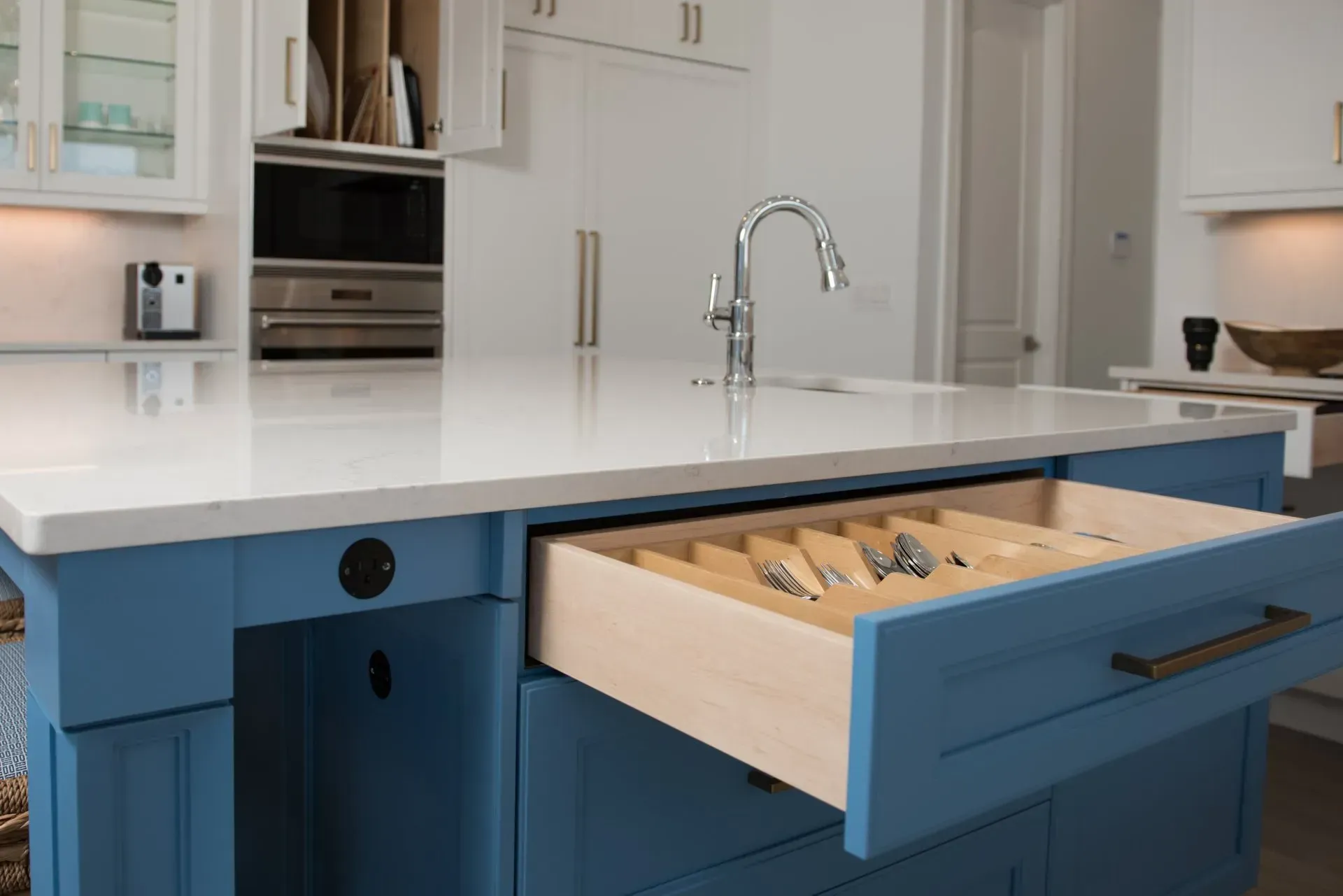 A kitchen with blue cabinets and a wooden drawer filled with utensils.