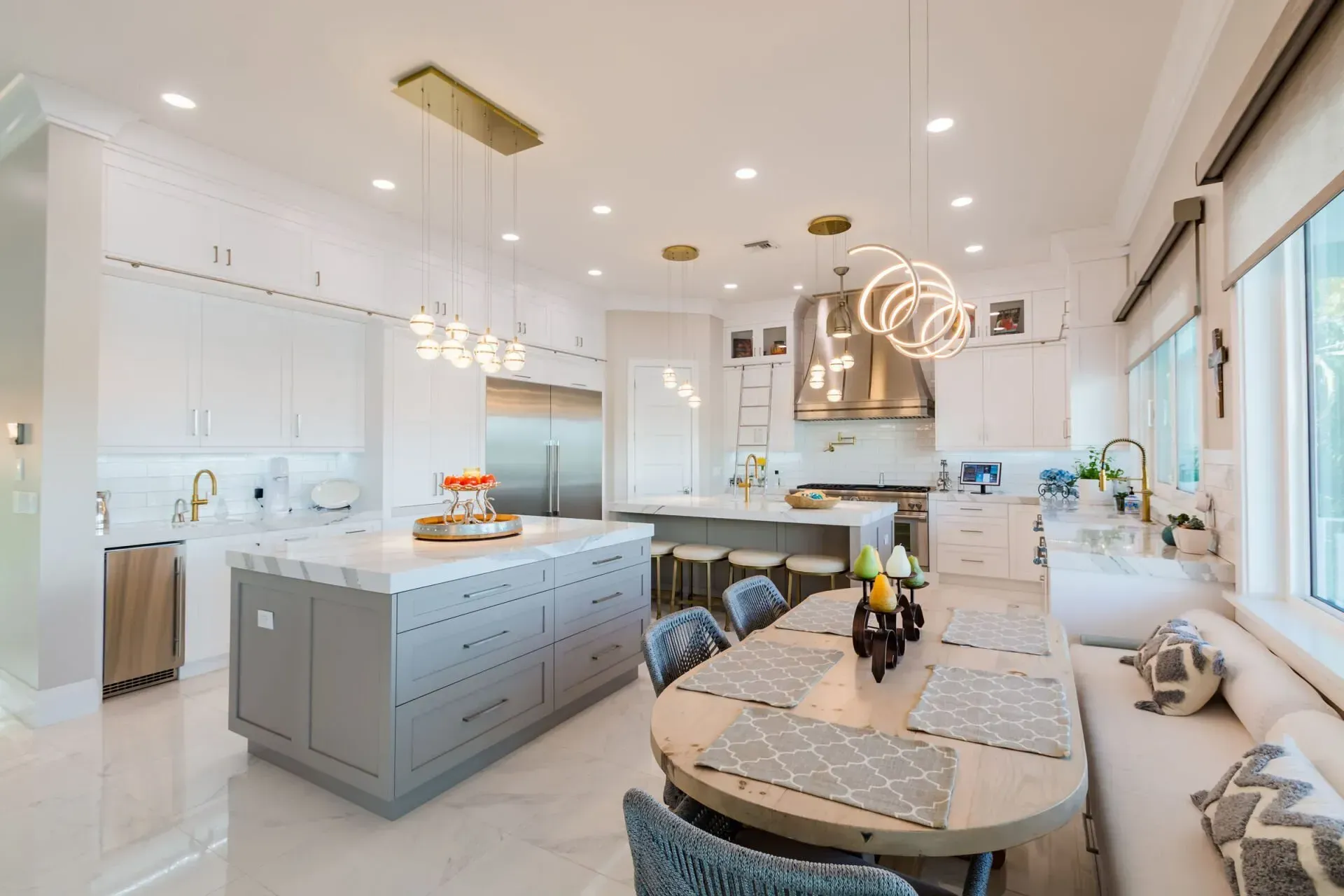 A kitchen with white cabinets , a large island , a table and chairs.
