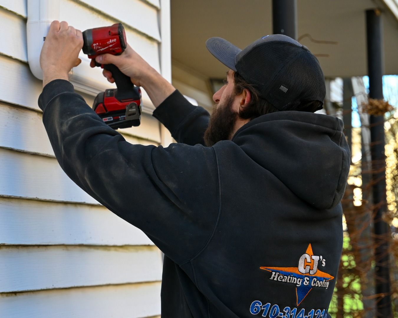 A man is working on the side of a house with a drill.