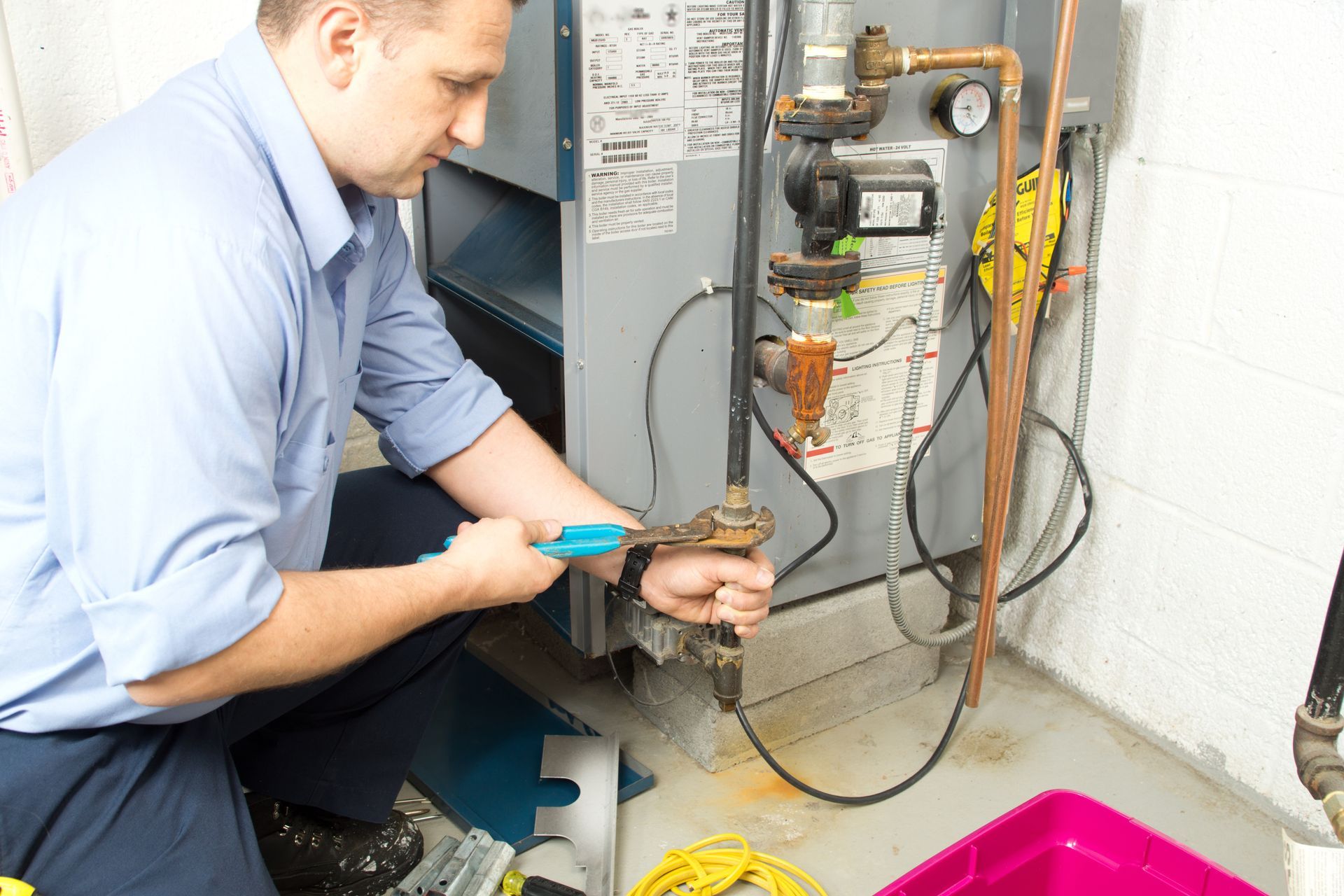 Technician kneeling by a furnace, using a tool to adjust wiring and components.