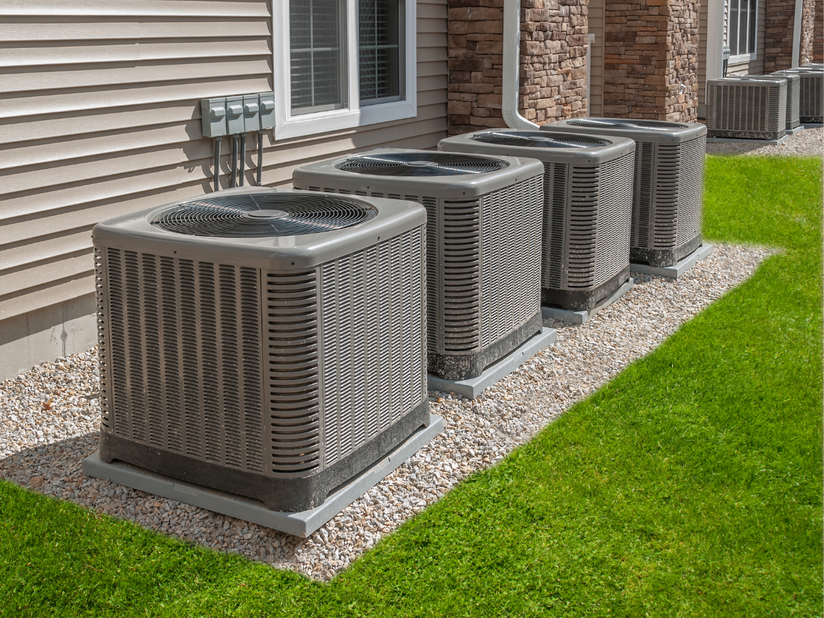 A row of air conditioners are sitting in front of a house.