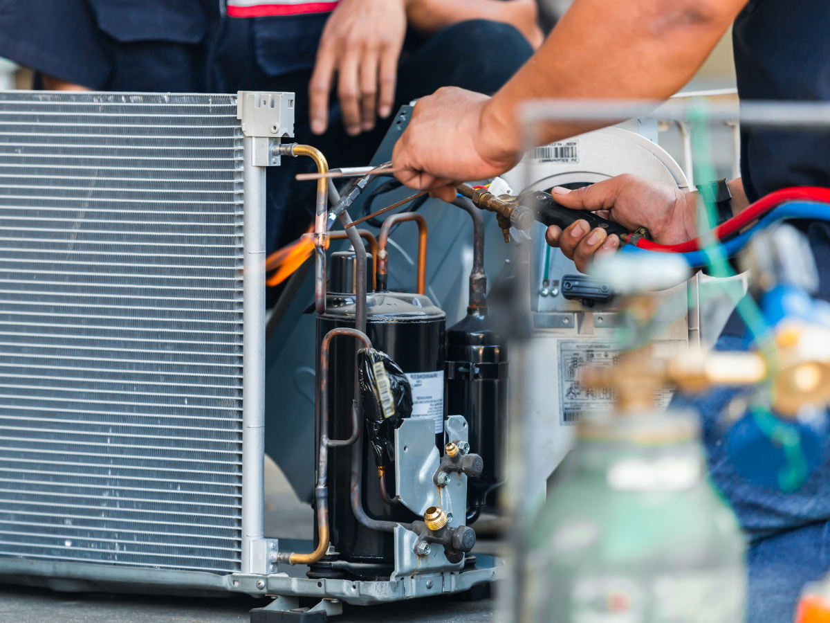 HVAC technician repairing an air conditioner with tools. Hands are visible, working near copper pipes and compressor. HVAC technician repairing an air conditioner with tools. Hands are visible, working near copper pipes and compressor.