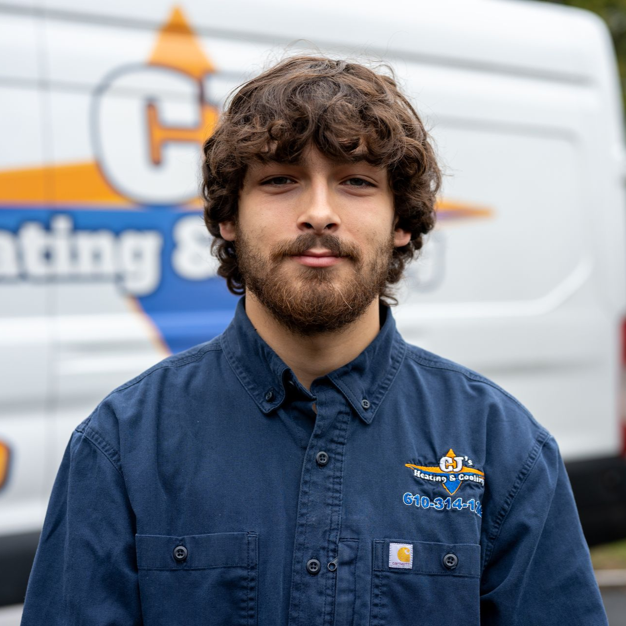 Young person in a navy work shirt standing in front of a white service van.