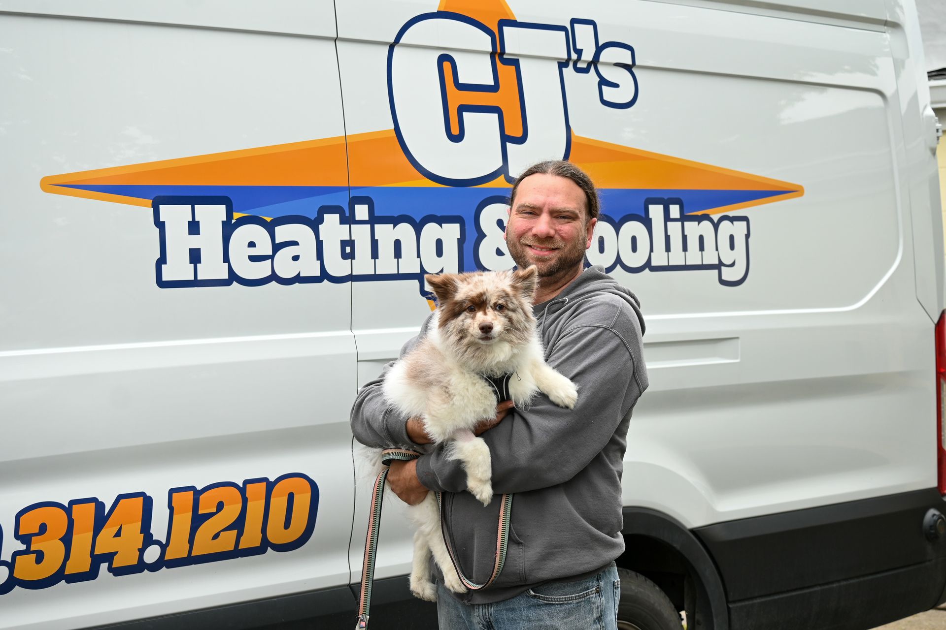 A man holding a dog in front of a heating and cooling van