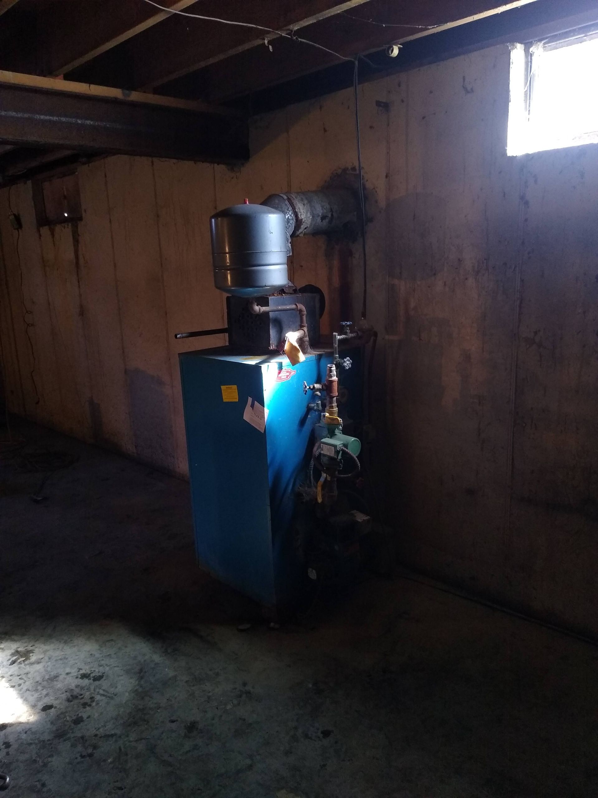 A blue boiler is sitting in a dark room next to a window
